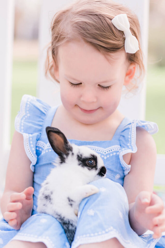 A toddler gently holding a baby rabbit at the farm
